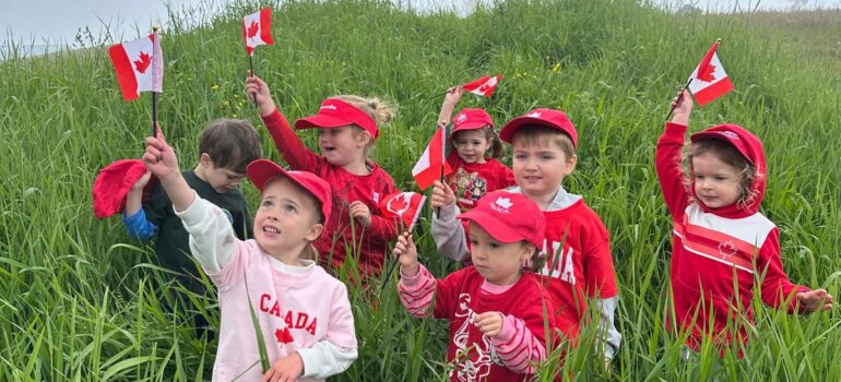 Daycare children wearing red hats and waving Canadian flags during an outdoor Canada Day activity