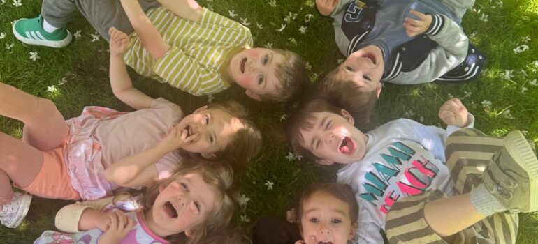 Children lying together on the grass during a fun outdoor daycare activity